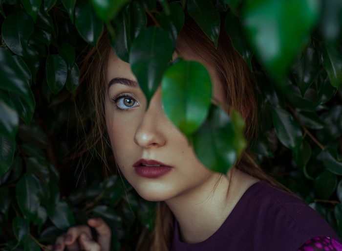 Woman peeking through green leaves