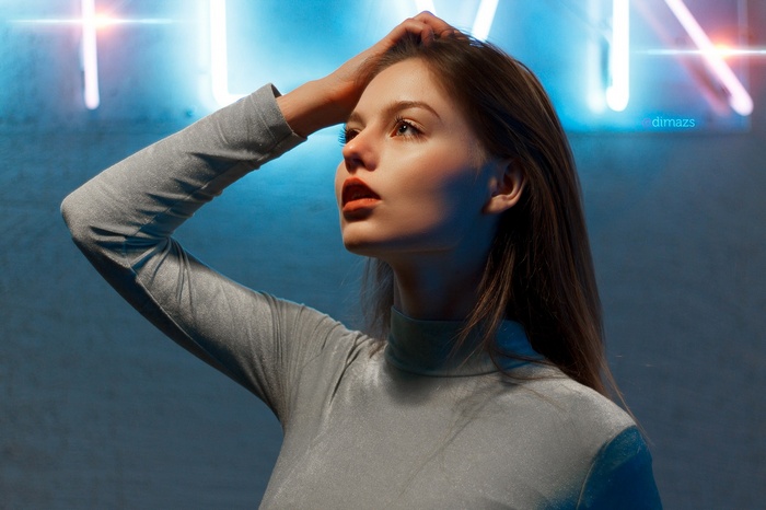 Woman with hand on head in front of neon lights