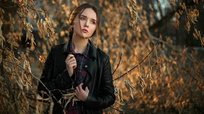 Woman in leather jacket and plaid shirt among dry branches