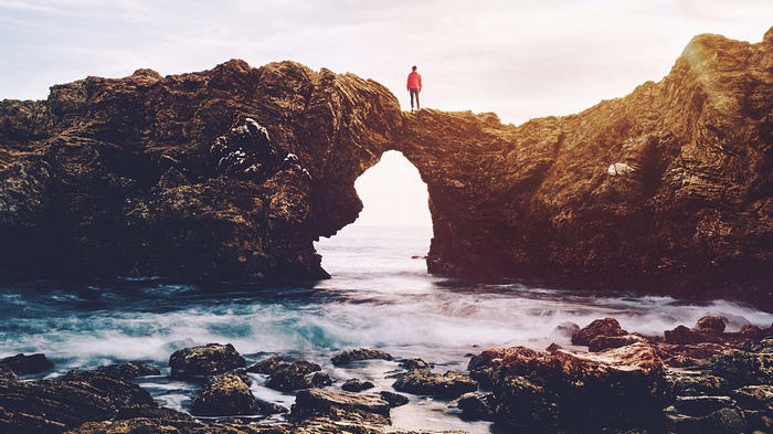Man standing on a rock arch over the ocean