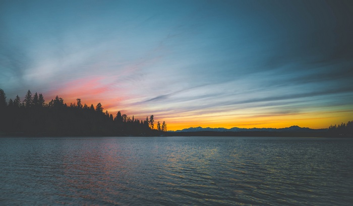 Sunset over a lake with silhouetted trees and mountains