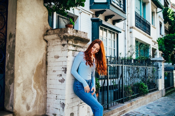 Redhead woman leaning against a brick wall outdoors