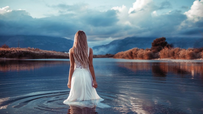 Woman in white dress standing in water with mountains in background
