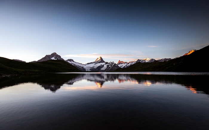 Lake reflecting snow-capped mountains at sunset