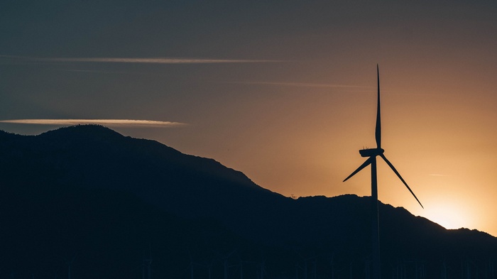 Silhouette of a windmill against a sunset over mountains