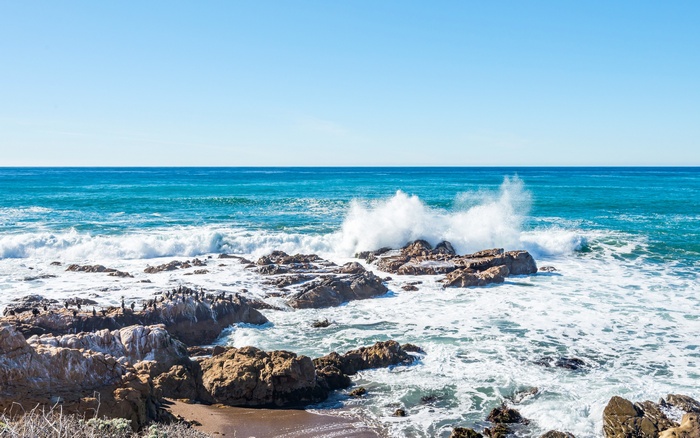 Waves crashing on rocky coast under clear blue sky