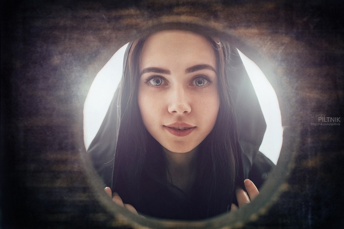 Woman wearing a black hood looking through a circular opening