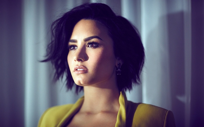Demi Lovato portrait with short dark hair and yellow jacket