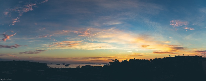 Sunrise over water with clouds and airplane contrail