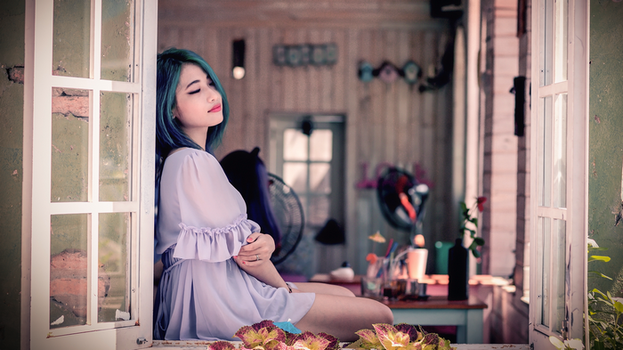 Woman with blue hair sitting by a window