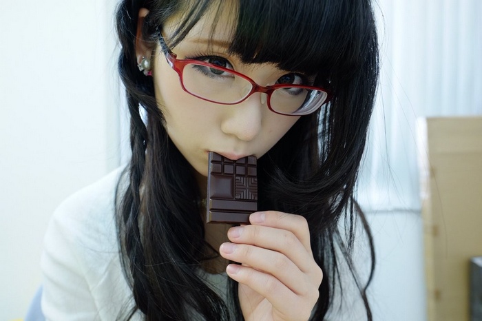 Japanese woman with black hair and red glasses eating chocolate