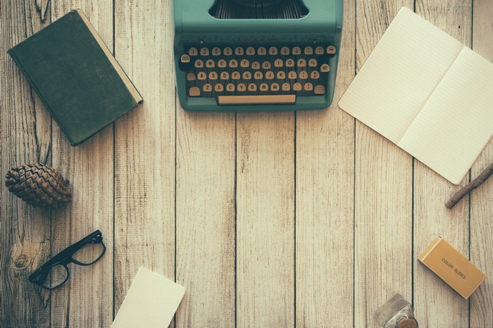 Vintage typewriter, books, glasses, and pine cone on wood