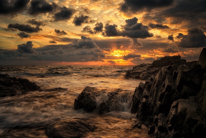 Sunset over the sea with dramatic clouds and rocky shore