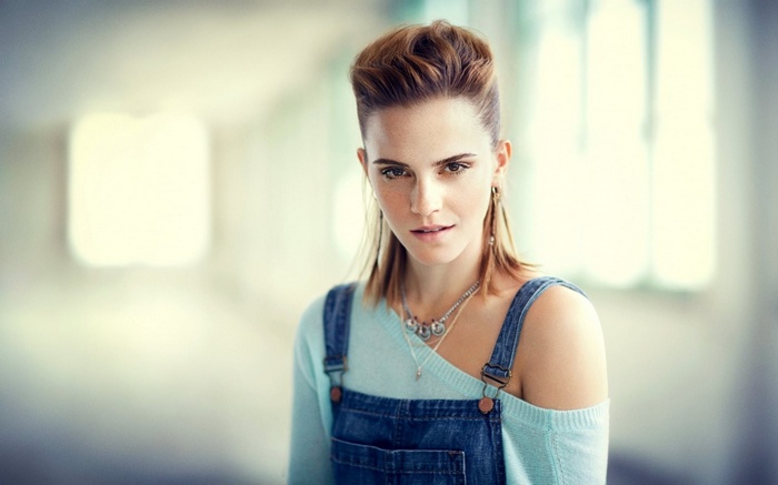 Emma Watson wearing denim overalls and a light blue sweater