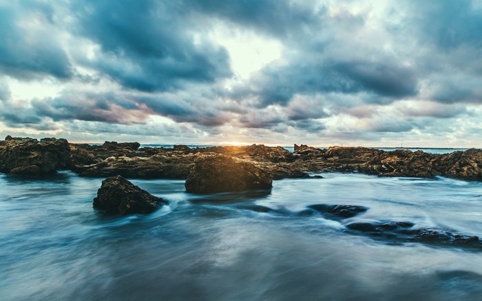 Rocky shore with waves at sunset under cloudy sky