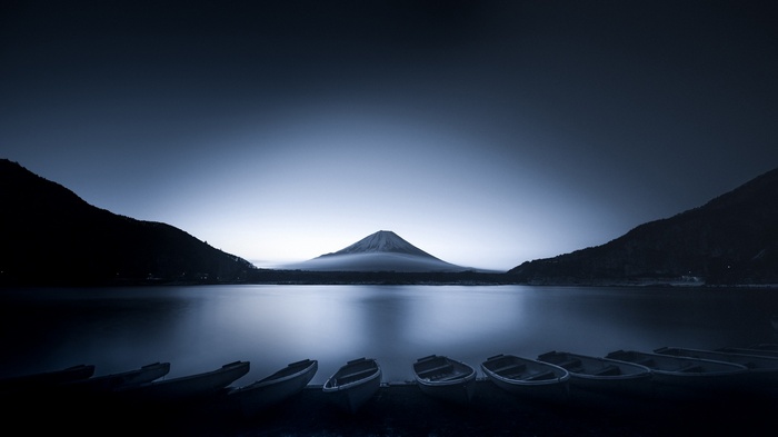 Mount Fuji over a calm lake with boats at sunrise