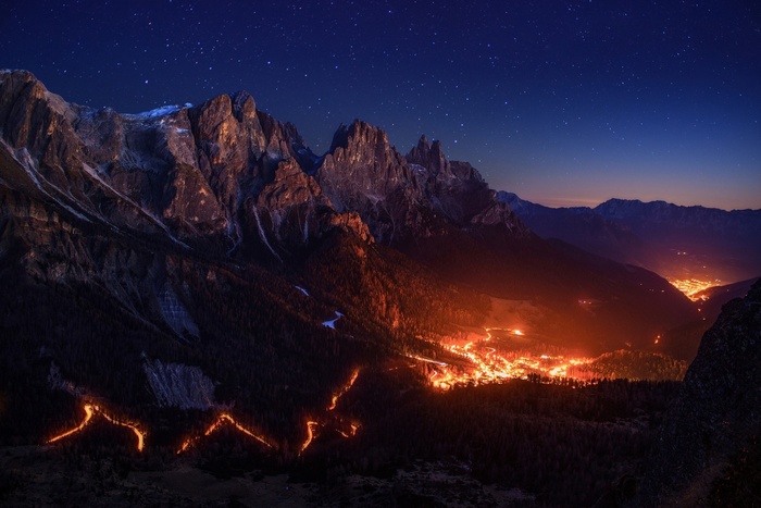 Mountain valley village at night with stars and fire lights