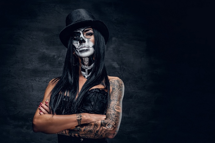 Woman with skull makeup and tattoos wearing a top hat