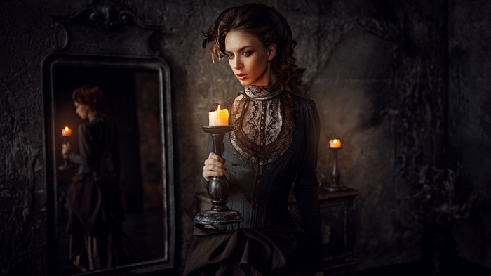 Woman in vintage dress holding a candle in front of a mirror