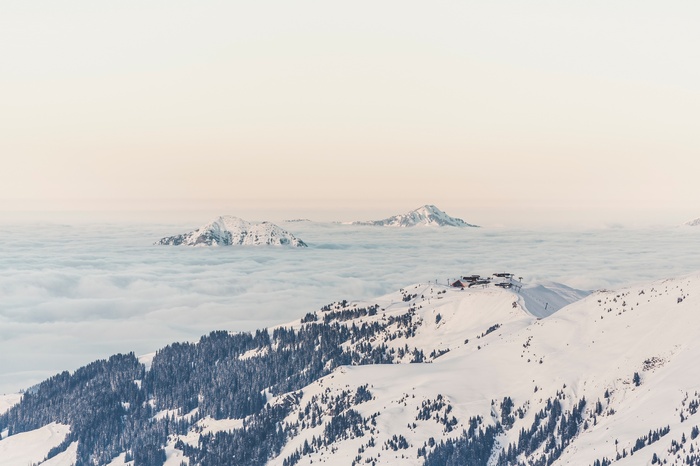 Snowy mountains above clouds with ski resort