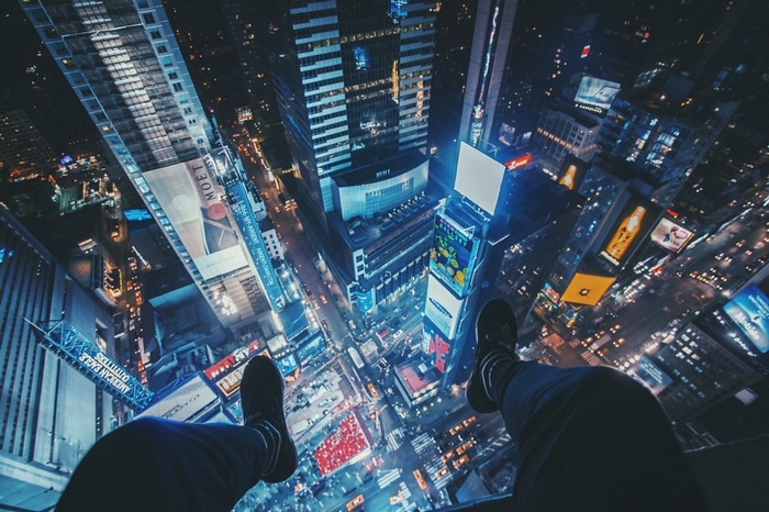 Person sitting on edge of skyscraper overlooking Times Square at night
