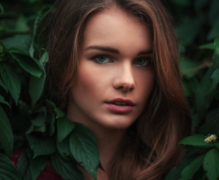 Woman with long brown hair surrounded by green leaves