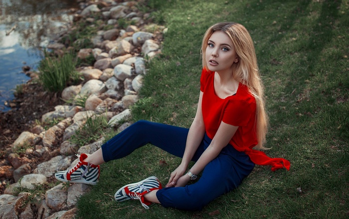 Woman in red top and blue pants sitting by rocks