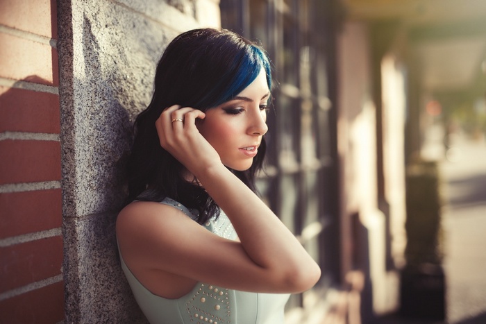 Woman with blue streaks in hair leaning against a wall