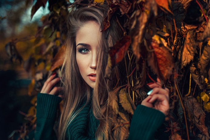 Woman with blonde hair behind autumn leaves