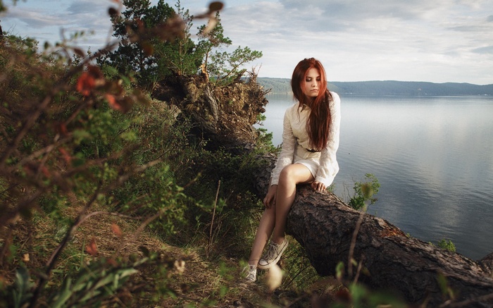 Redhead woman sitting on a fallen tree by a lake