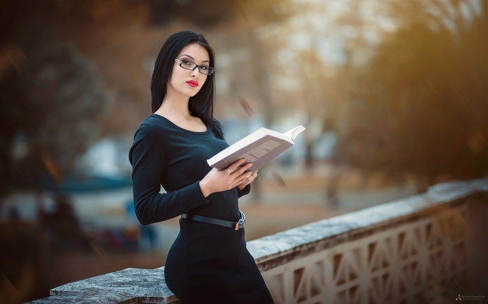 Woman wearing glasses and black dress reading a book outdoors