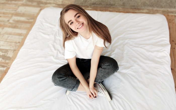 Woman in T-shirt and Jeans Sitting on a Bed