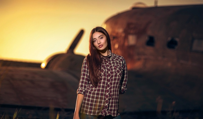 Woman in plaid shirt in front of airplane at sunset