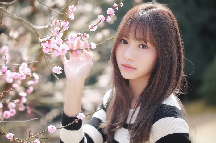 Young Asian woman with long hair among pink cherry blossoms