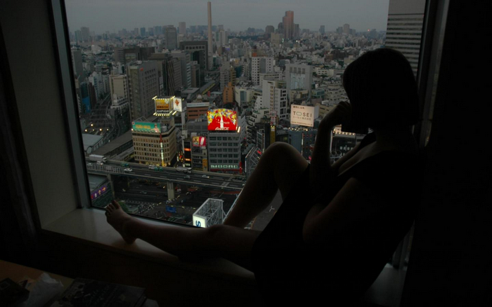 Woman sitting by window overlooking Tokyo cityscape at dusk