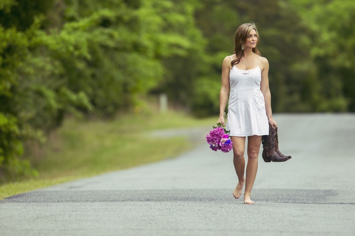 Woman in white dress walking barefoot with flowers and boots