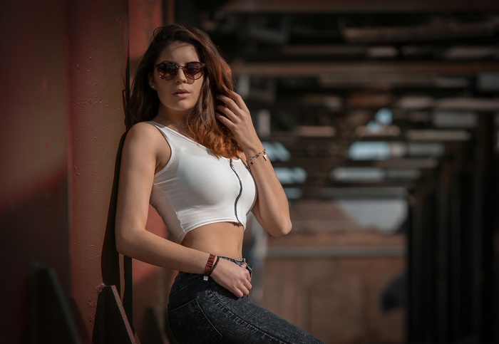 Woman in sunglasses and crop top leaning against wall