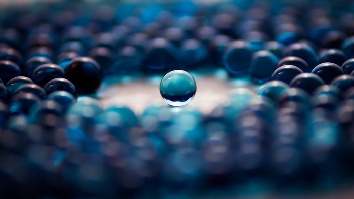 Abstract blue marbles with one clear marble in focus