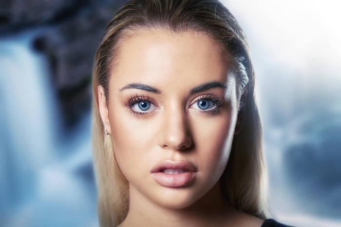 Woman with blue eyes and blonde hair in front of waterfall