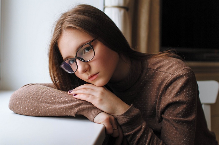 Young woman with glasses resting her head on her arms