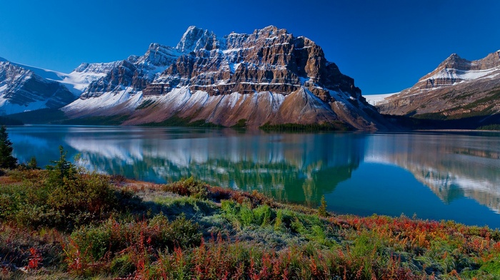 Snow-capped mountains reflected in a calm lake with colorful foliage