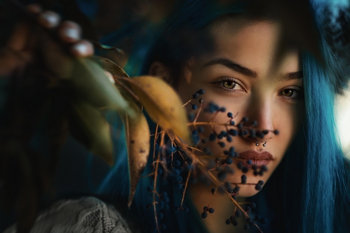 Woman with blue hair and nose ring behind leaves