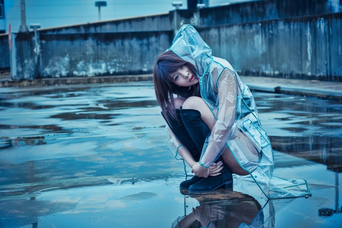 Asian woman in raincoat crouching in rain