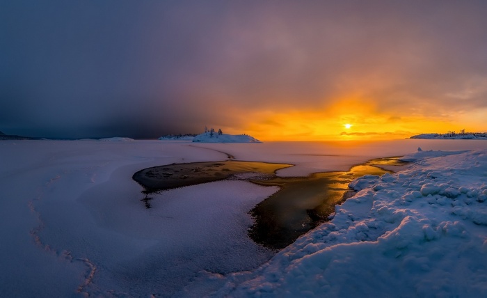 Winter sunset over a frozen lake with snow-covered land