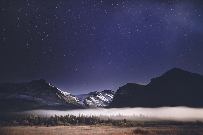 Mountains under a starry sky with mist and forest