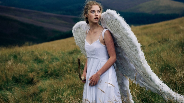 Woman with angel wings and bow in a grassy field