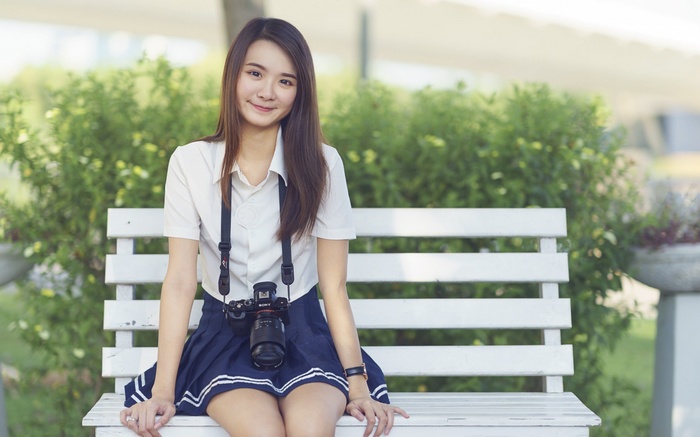 Asian schoolgirl with camera sitting on a bench