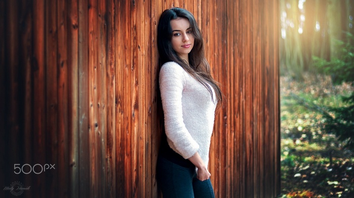 Woman in sweater and leggings leaning against wooden wall