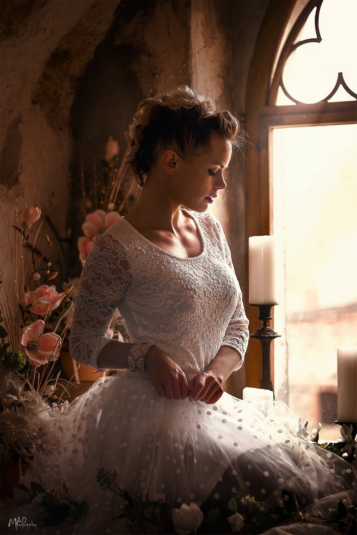 Woman in white lace dress by window with flowers and candles
