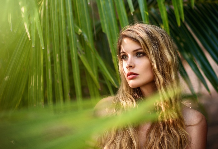 Woman with blonde wavy hair among palm leaves